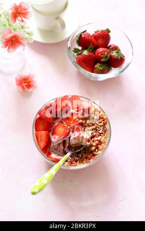 Frühstückskonzept. Eine Schüssel mit Müsli, Erdbeere, Joghurt isoliert auf weißem Hintergrund mit Nuancen von rosa. Kopierbereich. Stockfoto