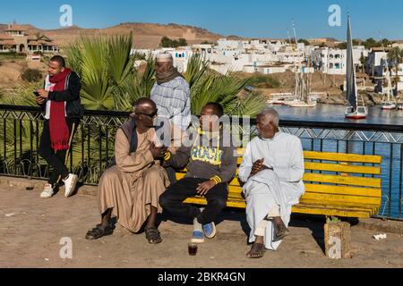 Ägypten, Oberägypten, Niltal, Assuan, nubische Männer in der Nähe des Nils mit nubischem Dorf im Hintergrund Stockfoto