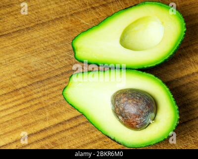 Eine halbierte Avocado mit dem Stein in einer Hälfte auf einem Holzhackbrett Stockfoto