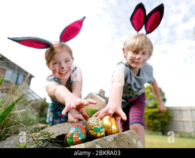 Ein Bruder und eine Schwester, die Gesichtsfarbe und hausgemachte Hasenohren tragen, nehmen an einer Ostereiersuche am Ostersonntag in ihrem Garten Teil. Stockfoto
