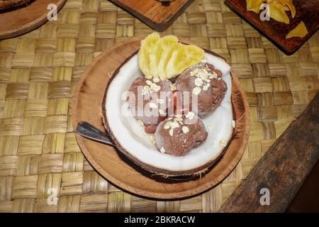 Schokoladeneis in frischer Kokosnuss mit Fleisch. Süßes Dessert mit Kakaoblätzchen, Bananenscheiben und Zimtstücken. Köstlich Stockfoto