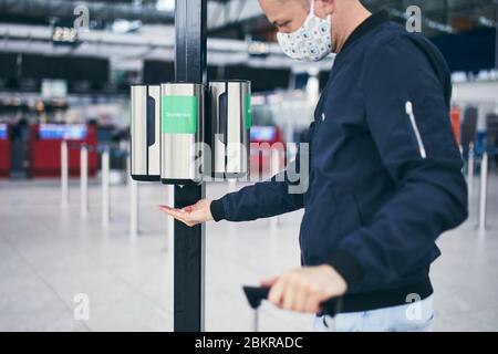 Mann, der eine Gesichtsmaske trägt und am Flughafen Handdesinfektionsmittel verwendet. Themen Reisen während der Pandemie, Hygiene und Personenschutz. Stockfoto