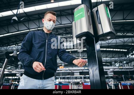 Mann, der eine Gesichtsmaske trägt und am Flughafen Handdesinfektionsmittel verwendet. Themen Reisen während der Pandemie, Hygiene und Personenschutz. Stockfoto