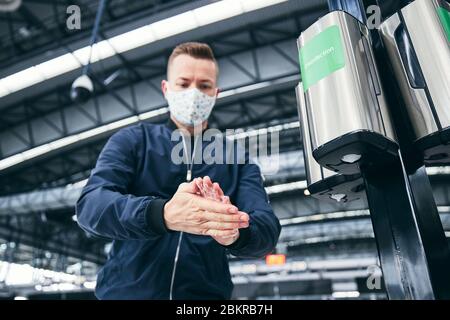 Mann, der eine Gesichtsmaske trägt und am Flughafen Handdesinfektionsmittel verwendet. Themen Reisen während der Pandemie, Hygiene und Personenschutz. Stockfoto