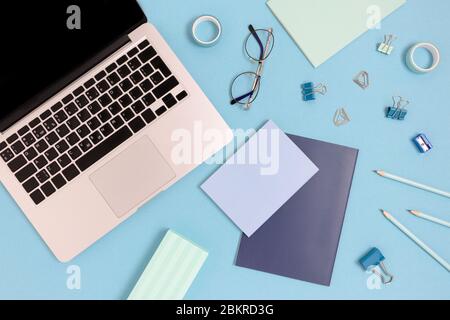 Flaylay von Laptop und Schreibwaren auf einem blauen Pastellgrund. Arbeitsplatzkonzept mit Büromaterial. Stockfoto