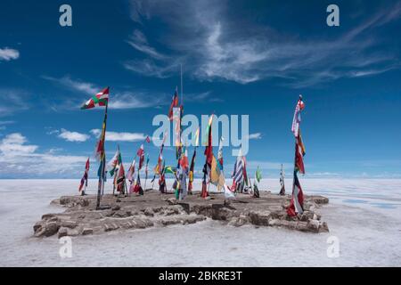 Ein Felsvorsprung auf den Salzebenen mit Flaggen vieler Länder unter einem blauen Himmel. Stockfoto