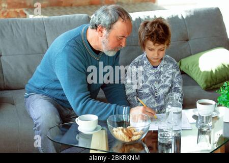 Nützliche Zeit. Großvater und sein Enkel verbringen Zeit zusammen isoliert zu Hause. Spaß haben, Stadtmachen, Lesen und Zeichnen. Konzept der Quarantäne, Familie, Liebe, Realismus, Zweisamkeit, Bildung. Stockfoto
