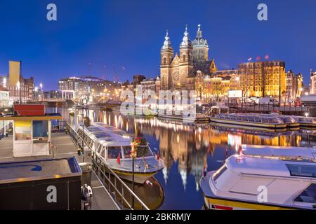 Amsterdam, Niederlande Blick ins Stadtzentrum mit Flussbooten und der Basilika St. Nikolaus bei Nacht. Stockfoto