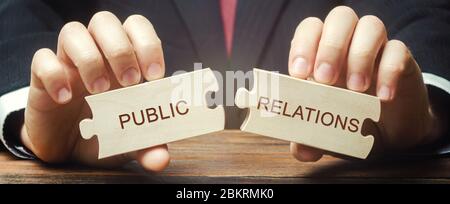 Geschäftsmann sammelt hölzerne Rätsel mit den Worten Public Relations. Verwaltung der Informationsflüsse zwischen der Organisation und der Öffentlichkeit. Sozial i Stockfoto
