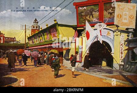 [ Japan der 1920er Jahre - Blick auf Asakusa, Tokio ] - Hanayashiki (浅草花やしき) in Asakusa, Tokio, eröffnet als Blumenpark im Jahr 1853 (Kaei 6). Als beliebtes Vergnügungszentrum beinhaltete es Teeläden, Unterhaltung und Tierausstellungen. 1949 (Showa 24) wurde es ein Vergnügungspark der Togo Company. Im Januar 2004 (Heisei 16) erklärte Togo den Konkurs und verkaufte Hanayashiki an Bandai, ein japanisches Spielzeugunternehmen. Der Turm im Hintergrund ist Ryunkaku (凌雲閣), Japans erster Wolkenkratzer. Es war im Volksmund bekannt als Asakusa Junikai (浅草十二階, Asakusa zwölf Geschichten). Vintage-Postkarte des 20. Jahrhunderts. Stockfoto