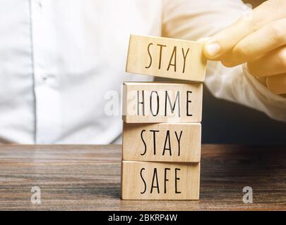 Mann setzt Holzblöcke mit den Worten zu Hause bleiben sicher. Das Konzept der Prävention von Coronavirus-Infektion. Selbstisolierung und Quarantäne. COVID- Stockfoto