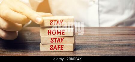 Mann setzt Holzblöcke mit den Worten zu Hause bleiben sicher. Das Konzept der Prävention von Coronavirus-Infektion. Selbstisolierung und Quarantäne. COVID- Stockfoto