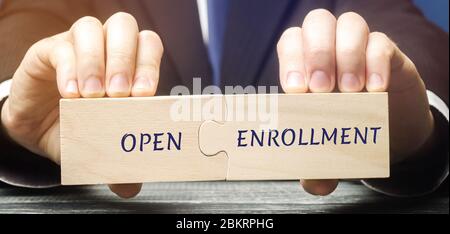 Geschäftsmann sammelt hölzerne Rätsel mit Worten Open Enrollment. Jährliche Periode der Versicherungsbeginn in den Vereinigten Staaten. Krankenversicherung, medicare. Stockfoto