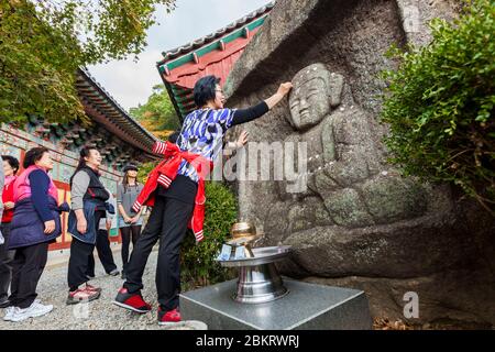 Südkorea, Südgyeongsang Provinz, Sanggyesa Tempel, koreanische Frauen, die Glücksmünzen auf eine Buddha-Skulptur legen Stockfoto