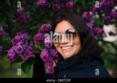 Porträt einer schönen Frau lächelnd im Park mit violetten lila Blumen Stockfoto