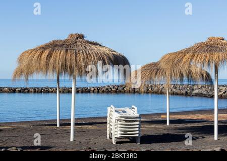 Strohhalm-Sonnenschirme an einem menschenleeren Strand Playa Beril während der Blockade 19 im touristischen Ferienort Costa Adeje, Teneriffa, Canar Stockfoto