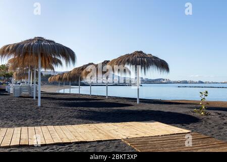 Strohhalm-Sonnenschirme an einem menschenleeren Strand Playa Beril während der Blockade 19 im touristischen Ferienort Costa Adeje, Teneriffa, Canar Stockfoto