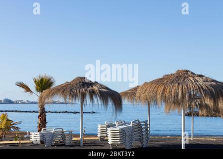 Strohhalm-Sonnenschirme an einem menschenleeren Strand Playa Beril während der Blockade 19 im touristischen Ferienort Costa Adeje, Teneriffa, Canar Stockfoto