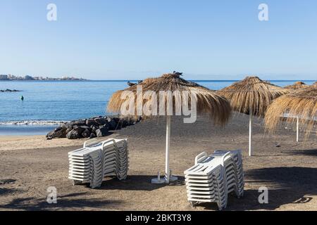 Strohhalm-Sonnenschirme an einem menschenleeren Strand Playa Beril während der Blockade 19 im touristischen Ferienort Costa Adeje, Teneriffa, Canar Stockfoto