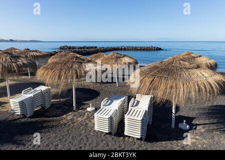 Strohhalm-Sonnenschirme an einem menschenleeren Strand Playa Beril während der Blockade 19 im touristischen Ferienort Costa Adeje, Teneriffa, Canar Stockfoto