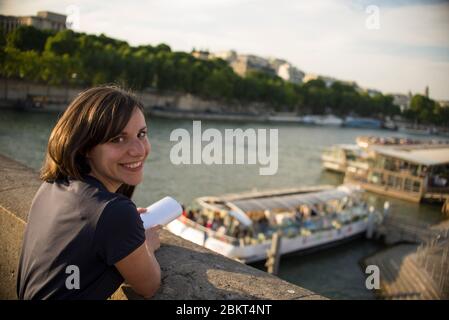 Junge lächelnde Touristen schaut lächelnd in die Kamera bei Sonnenuntergang am Ufer der seine in Paris. Stockfoto