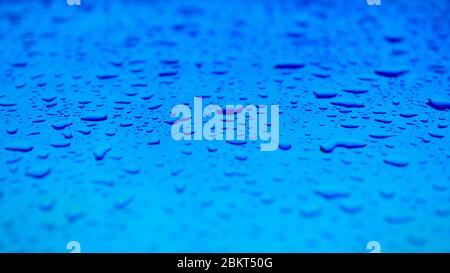 Wasser tropft auf die blaue Oberfläche. Schöner farbenfroher Hintergrund mit geringer Schärfentiefe. Frischekonzept Foto. Breites Webformat. Stockfoto