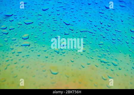 Wassertropfen auf der holographischen Chamäleon-Oberfläche. Schöner farbenfroher Hintergrund mit geringer Schärfentiefe. Blauer und gelber Farbverlauf. Stockfoto