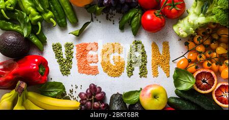 Banner der Inschrift VEGAN aus Linsen verschiedener Arten und Farben. Frisches Gemüse und Obst auf einem weißen Küchentisch. Hintergrund für Supermark Stockfoto