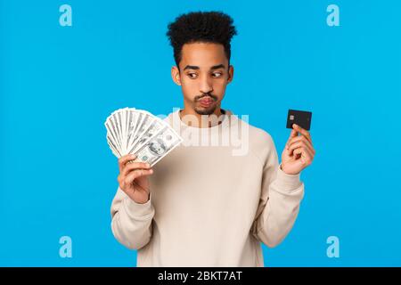 Unentschlossenen und gestörten jungen african-american Kerl mit Blick auf harte Entscheidung, schmollen, ausatmen harte Wahl Macht, Geld und Kreditkarte, betrachten Stockfoto