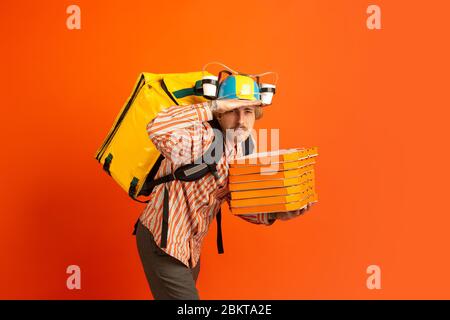 Suche nach Kunden. Emotionen des kaukasischen Deliveryman isoliert auf orangefarbenem Hintergrund. Kontaktloser Lieferservice während der Quarantäne. Der Mensch liefert Nahrung während der Isolation. Sicherheit. Schnell nach oben. Stockfoto