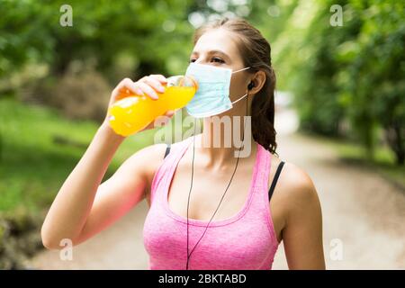 Junge maskierte Frau nach Sport während Coronavirus Pandemie trinken, lustiges Konzept Stockfoto