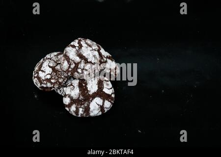 Hausgemachte Kekse mit Schokoladenchips mit Puderzucker auf schwarzem Hintergrund. Frisch gebackener Schoko-Keks aus nächster Nähe. Dunkles Essen. Kochen Sie zu Hause. Stockfoto