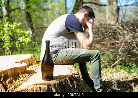 Ein unglücklicher Mann löst Probleme mit Alkohol. Traurig und allein mit einer Flasche Alkohol in der Natur Stockfoto