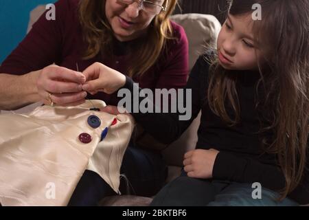 Die liebevolle Großmutter lehrt ihre kleine Enkelin, wie man Knöpfe näht Stockfoto