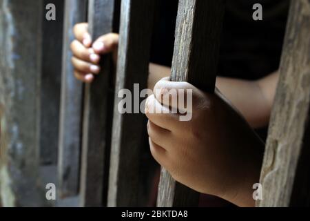 Hände eines kleinen Kindes, das die Gefängnisstangen festklammert. Kind im Gefängnis. Trauriger kleiner Junge gezwungen, zu Hause zu bleiben, wie das pandemische Coronavirus, covid19. Stockfoto