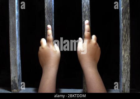 Hände eines kleinen Kindes, das die Gefängnisstangen festklammert. Kind im Gefängnis. Trauriger kleiner Junge gezwungen, zu Hause zu bleiben, wie das pandemische Coronavirus, covid19. Stockfoto