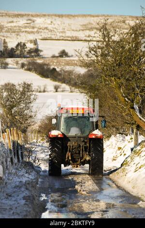 Pontypridd, Wales - Dezember 2017: Bauernhof Traktor fahren auf einer schneebedeckten Landstraße im Winter Stockfoto