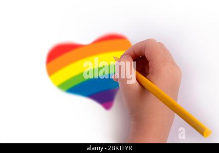 Das Konzept der Verfolgung des Regenbogens. Eine Hand mit einem Bleistift zeichnet ein Herz in Regenbogenfarben. Stockfoto