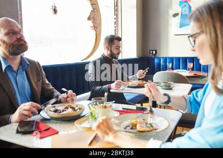 Ein hübscher junger Geschäftsmann, der Salat isst und im modernen Café telefoniert Stockfoto