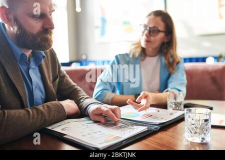 Nahaufnahme eines nachdenklichen bärtigen Geschäftsmannes, der Graphen und Diagramme mit Kollegen in einem modernen Café analysiert Stockfoto