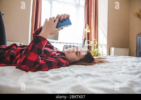 Langweilige Frau, die mit dem Handy im Bett lag. Stockfoto