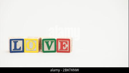 Kleine hölzerne Spielzeugblöcke buchstabieren das Wort Liebe in bunten Buchstaben auf einem weißen Hintergrund. Stockfoto