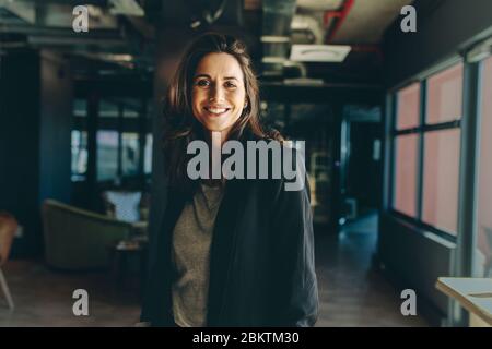 Lächelnde weibliche Führungskraft im Büro. Frau in formeller Geschäftskleidung schaut Kamera an und lächelt. Stockfoto