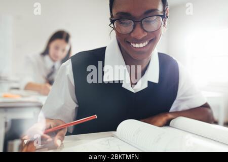 Teenager-Mädchen mit Brille sitzen am Schreibtisch im Klassenzimmer in der High School. Studentin lächelnd während des Studiums im Klassenzimmer.