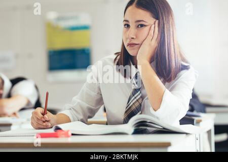 Teenager-Mädchen in Uniform sitzen am Schreibtisch im Klassenzimmer und denken. Studentin beim Denken im Klassenzimmer. Stockfoto