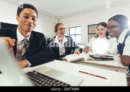 Gruppe von Studenten, die zusammen auf einem Laptop im Klassenzimmer lernen. Jungen und Mädchen in Uniform, die an einem Schulauftrag arbeiten. Stockfoto