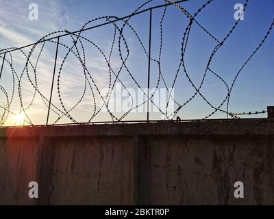 Gefängnismauern mit Stacheldraht auf einem Sonnenuntergang Hintergrund. Betonzaun mit Stacheldraht. Stockfoto