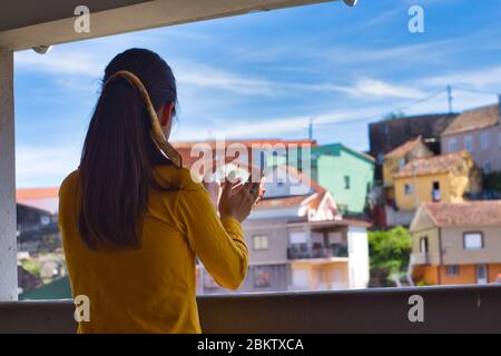 Junge Frau klatscht auf dem Balkon mit den Händen, um allen Beschäftigten im Gesundheitswesen während des Coronavirus-Ausbruchs Dankbarkeit zu zeigen. Viele bunte Häuser. Stockfoto