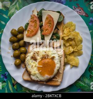 Ein Gericht mit Spiegelei mit Käse und Pfeffer auf Brotscheiben, Tomaten, Käse, Chips, Oliven und Gemüse Stockfoto