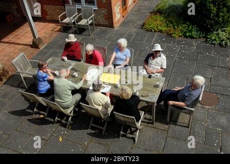 Eine Gruppe von neun Rentnern, die an einem Tisch sitzen und sich bei Sonnenschein unterhalten. Stockfoto